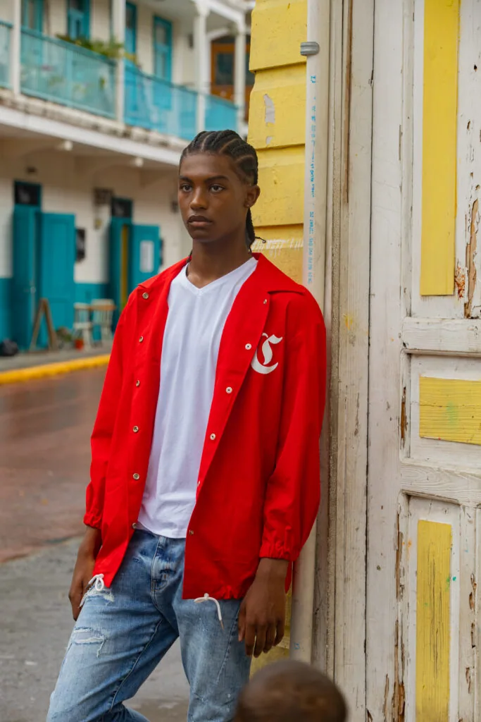 Male model in red jacket and white shirt standing against yellow colonial building with blue doors