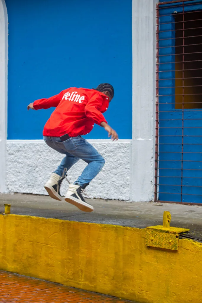 Man in red jacket jumping over yellow barrier against blue wall with white column