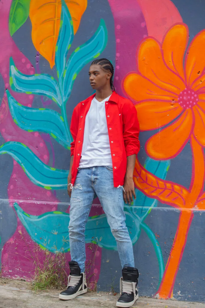 Young male model in red jacket and light jeans standing before colorful floral street art mural