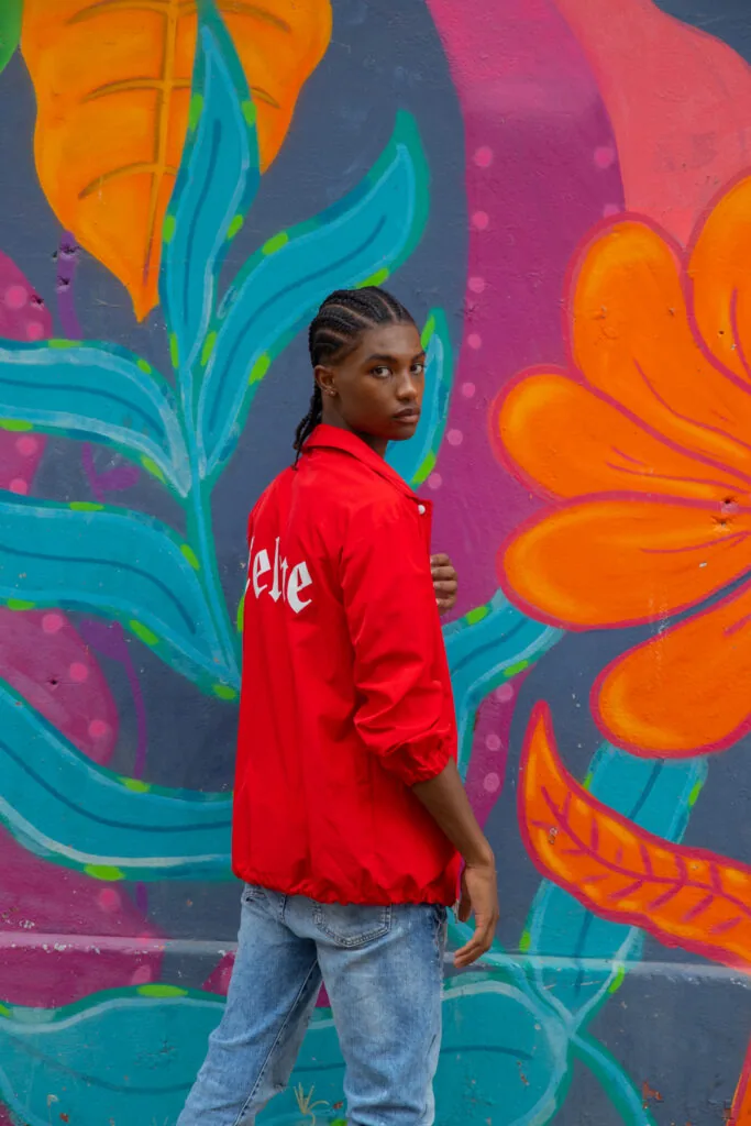 Male model in red jacket and jeans posing against vibrant colorful floral street art mural