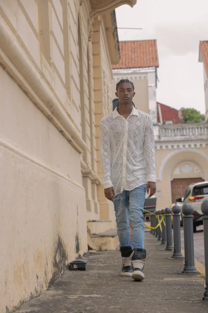 Male model in white patterned shirt and jeans walking on narrow European street with historic buildings