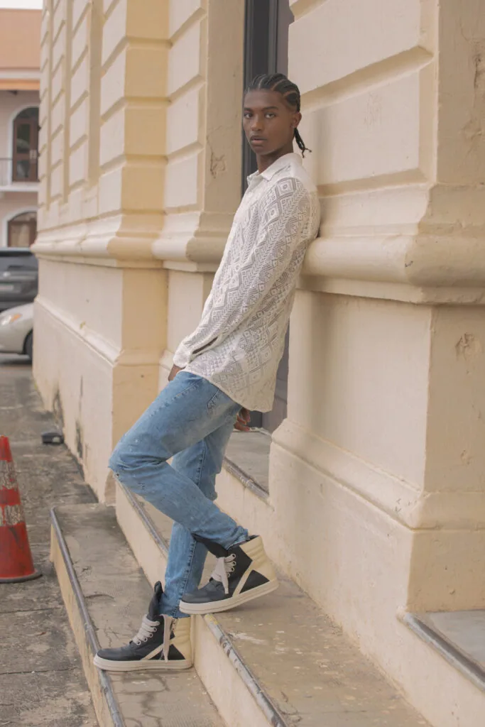 Male model in cream cable-knit cardigan and blue jeans posed against architectural building facade with geometric details
