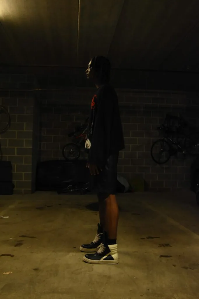 Man in black jacket and shorts standing in parking garage with bicycles in background at night