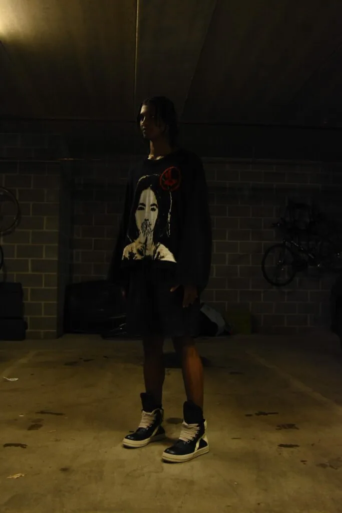 Male model wearing graphic portrait t-shirt and black sneakers in industrial brick garage setting