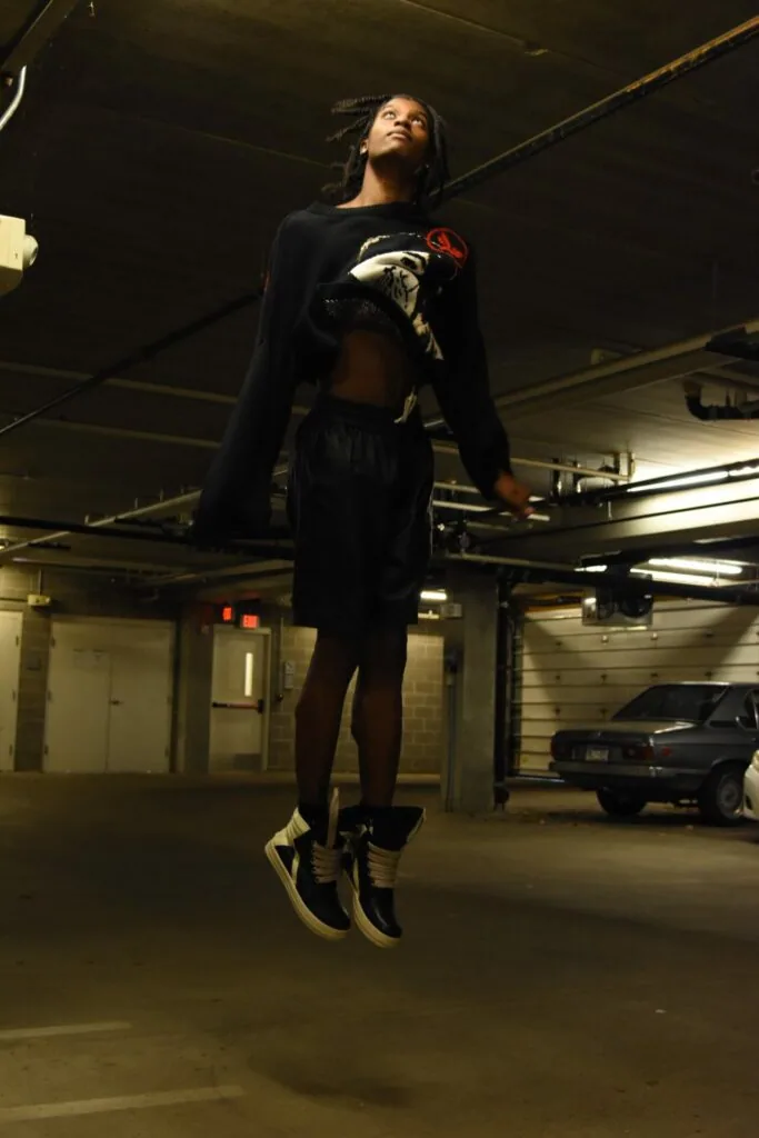 Person in black crop top and skirt with black and gold sneakers jumping in underground parking garage