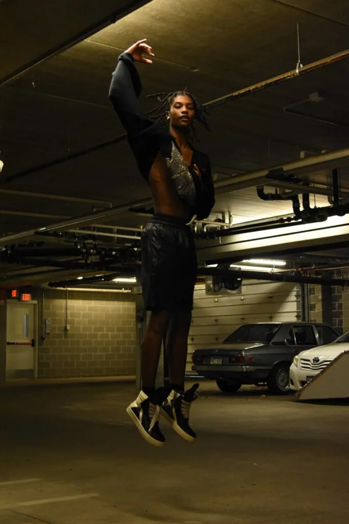 Male model jumping in underground parking garage wearing black blazer and shorts with two-tone sneakers