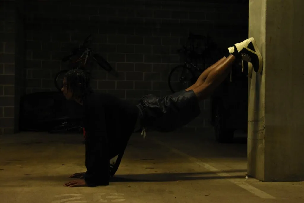 Male model in black outfit performing athletic pose against concrete wall in industrial garage setting