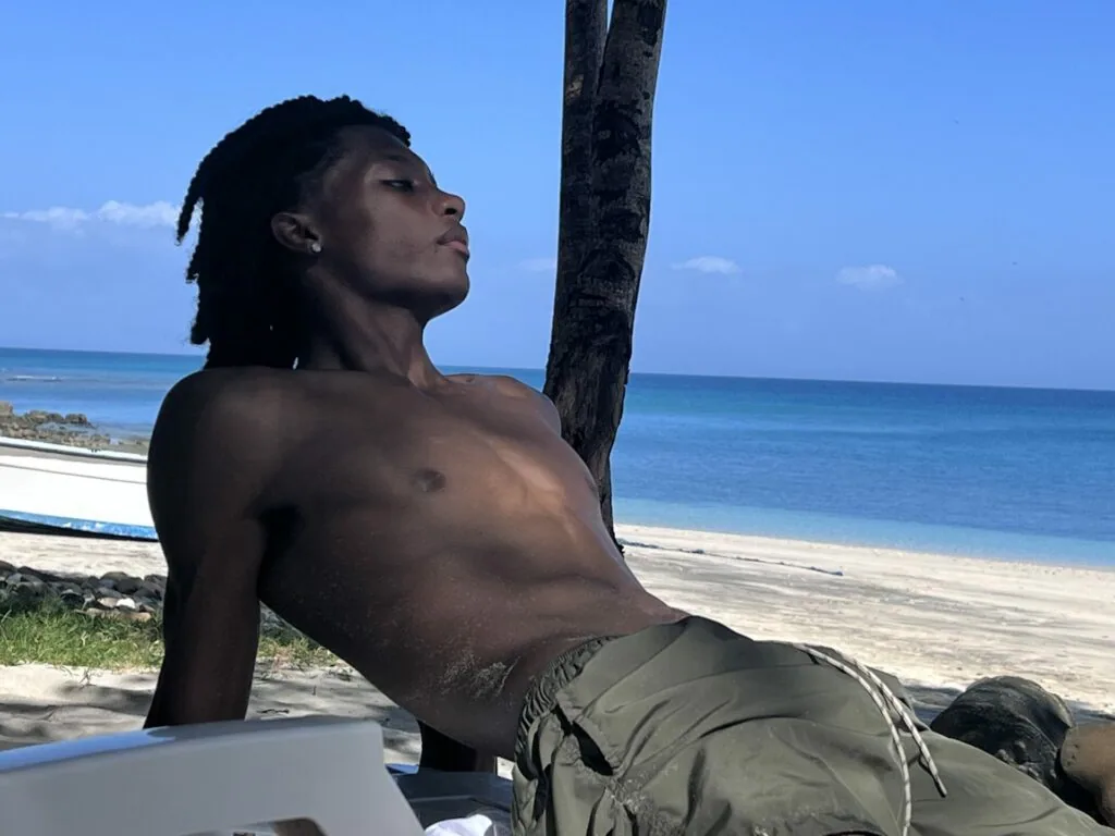 Shirtless man relaxing against palm tree on tropical beach with ocean view