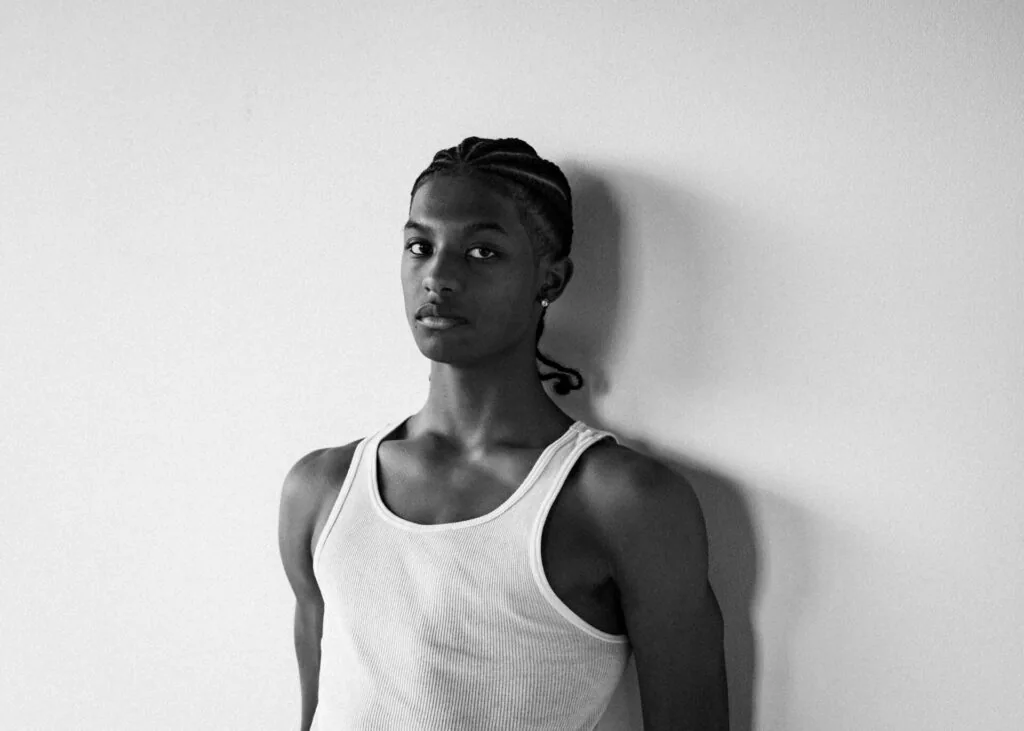 Male model in white ribbed tank top against white wall, black and white portrait photography