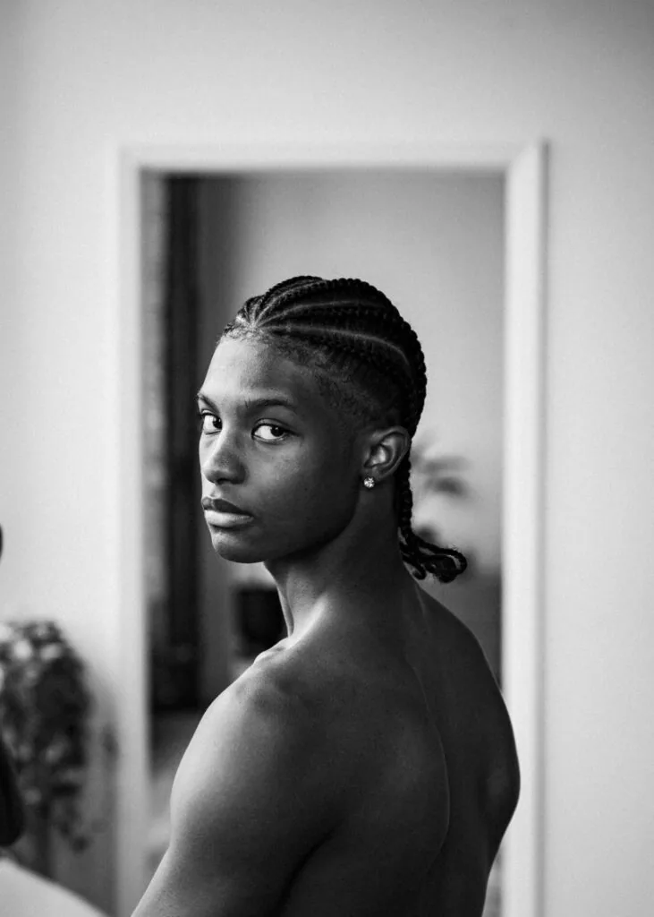Male model with braided hair wearing earring, shot in black and white profile against white doorway