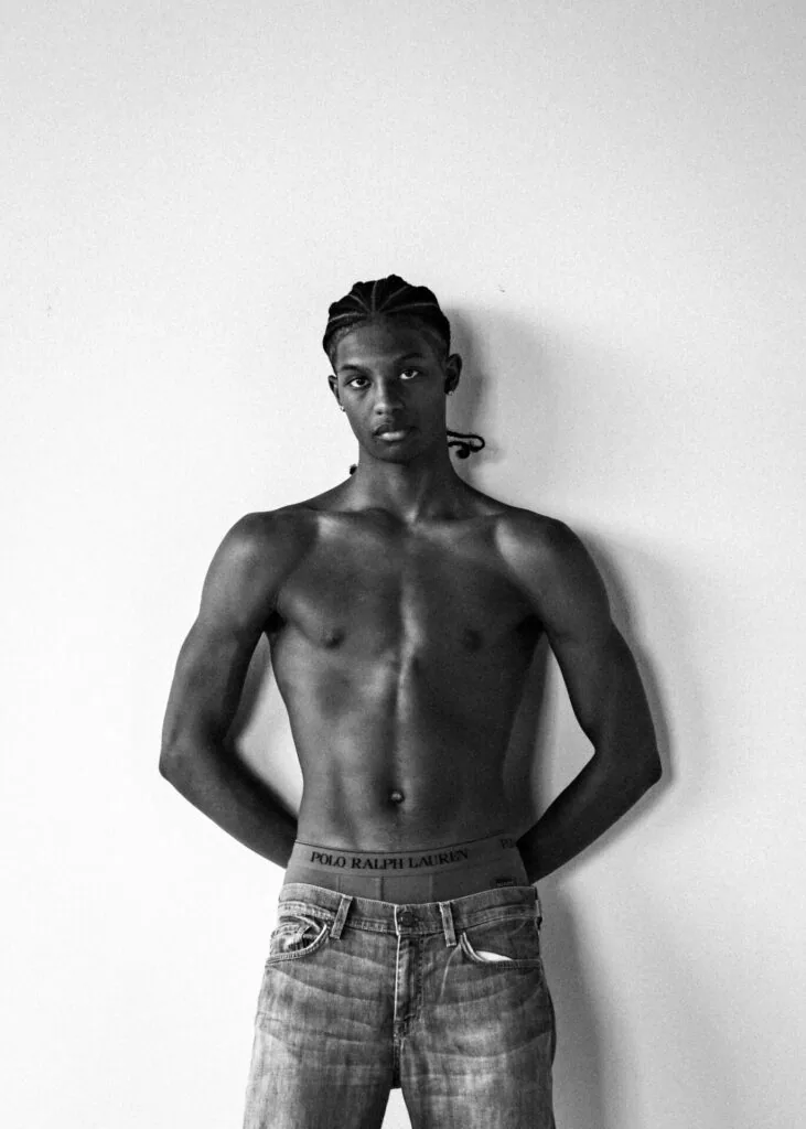 Shirtless male model in designer waistband and jeans against white backdrop, studio portrait