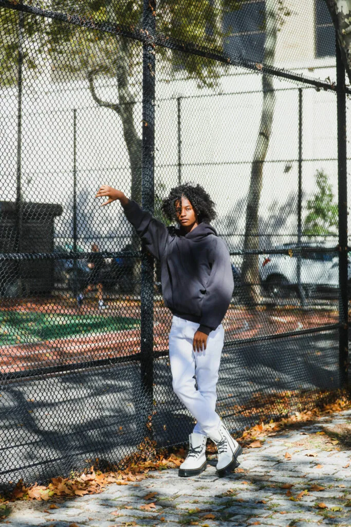 Man in black hoodie and white sweatpants posing inside tennis court with chain-link fence