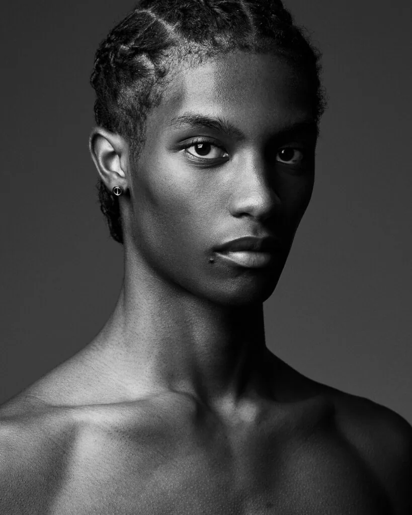 Male model with shaved head and ear piercing against gray studio background, professional headshot