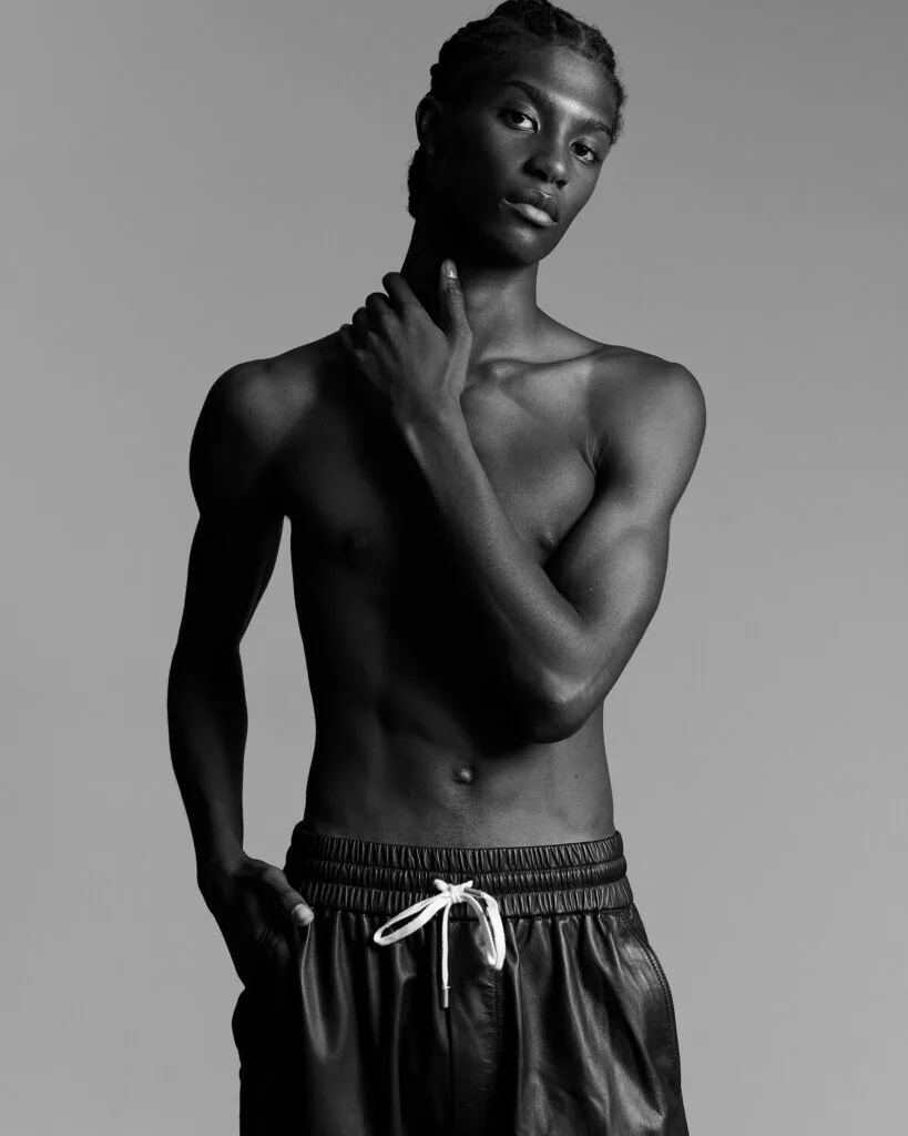 Shirtless male model in black drawstring pants posing against gray studio background