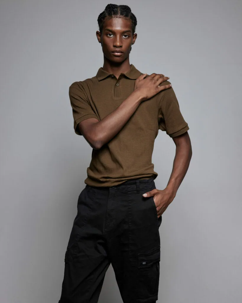 Male model wearing olive polo shirt and black cargo pants, hand on shoulder, studio portrait