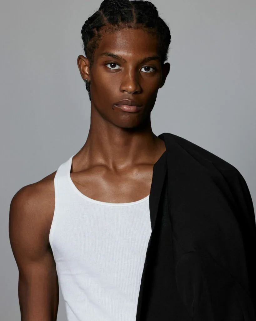 Male model wearing white tank top and black cardigan against gray background