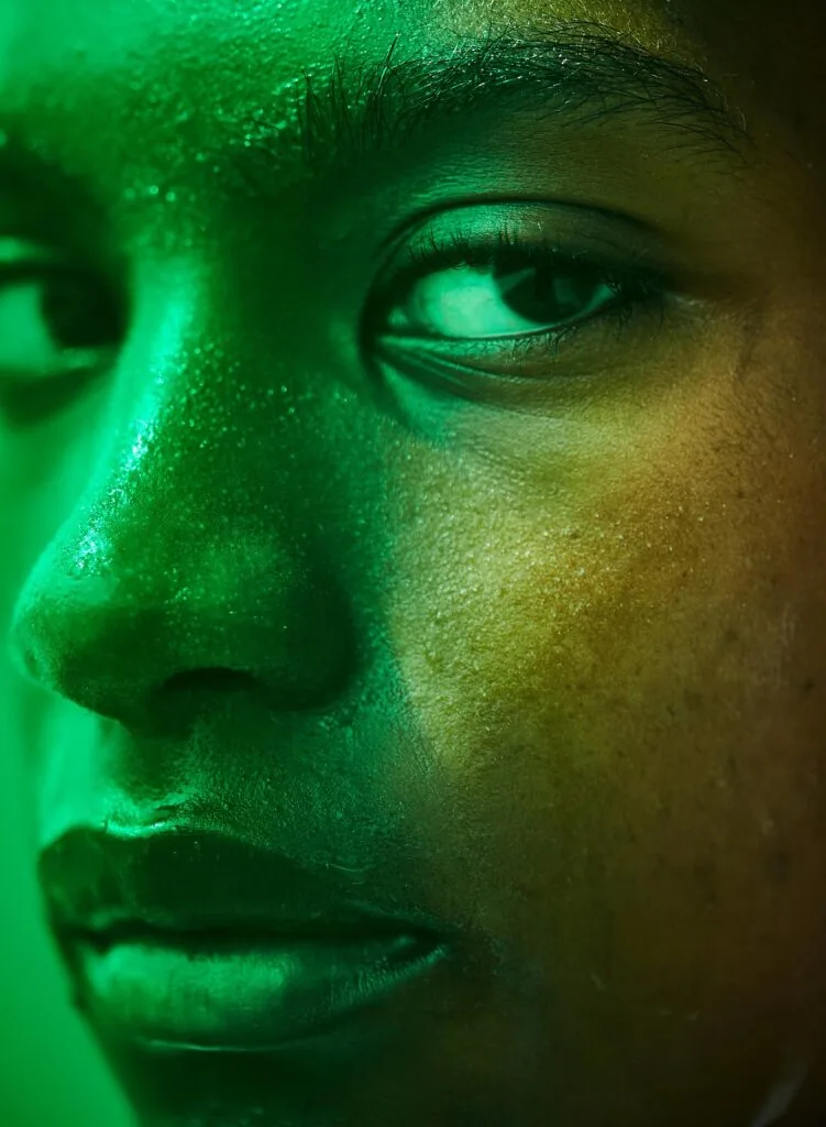 Male model's face in profile with green and yellow monochromatic lighting, showcasing cheekbone and eye detail
