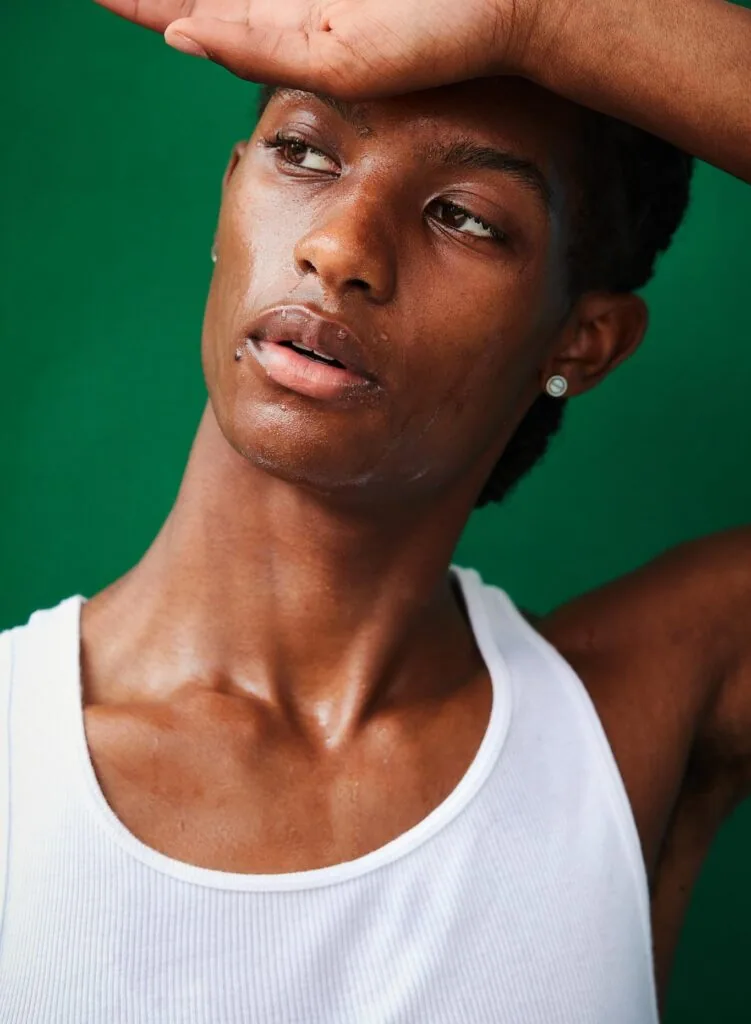 Male model wearing white tank top with hand to head against green background