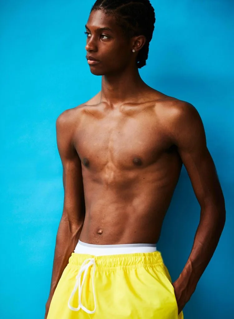 Shirtless male model in yellow swim shorts against bright blue background