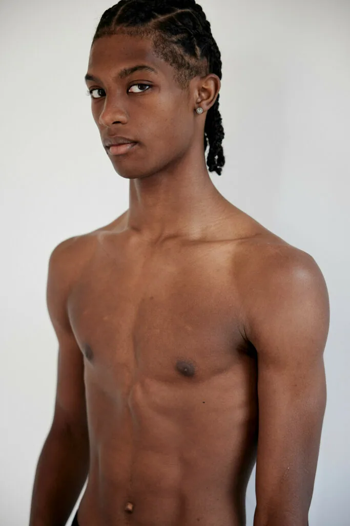 Shirtless male model with braided hair in three-quarter pose against white background