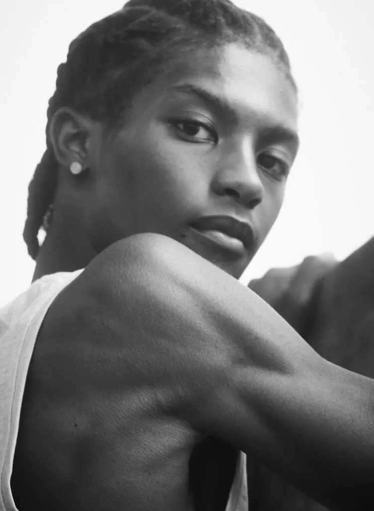 Male model in white tank top wearing pearl earring, black and white portrait against neutral background