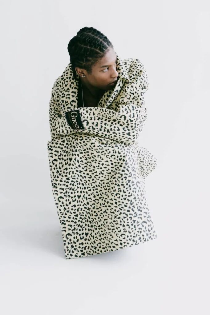 Male model in leopard-print coat with braided hair against white background