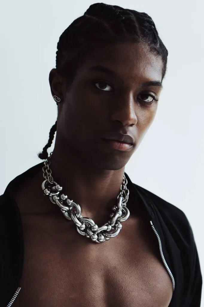 Male model wearing black open shirt and silver chain necklace against white background