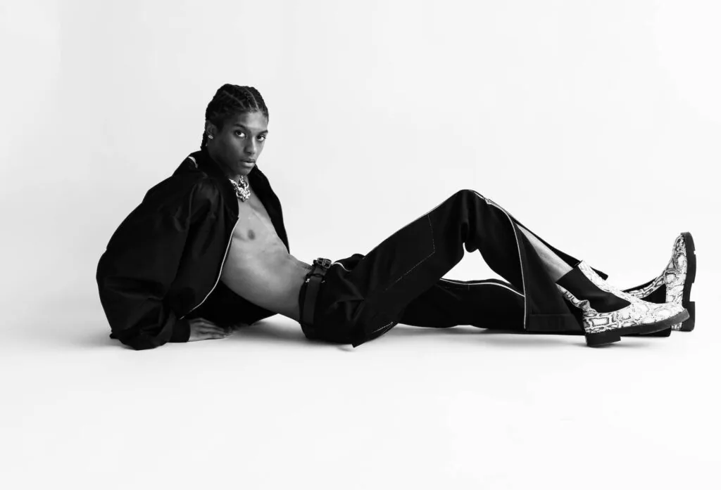 Male model in black blazer and patterned boots reclining on white background, professional fashion portrait