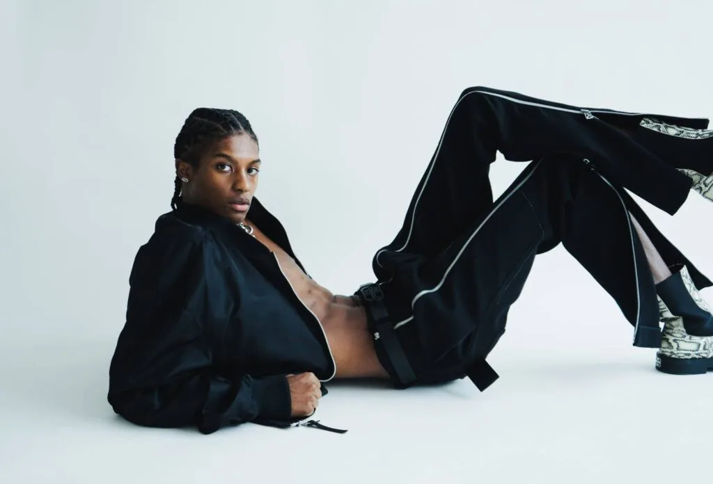 Male model in black oversized blazer and trousers reclining on white background with confident pose