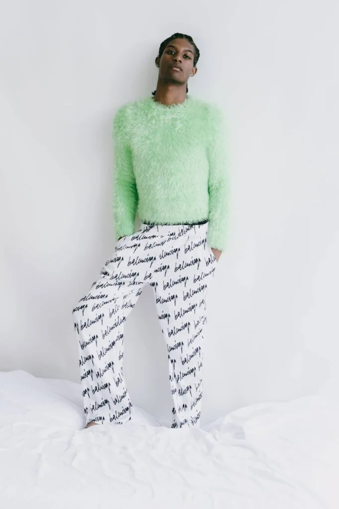 Male model wearing lime green fuzzy sweater and white text-printed pants against white background