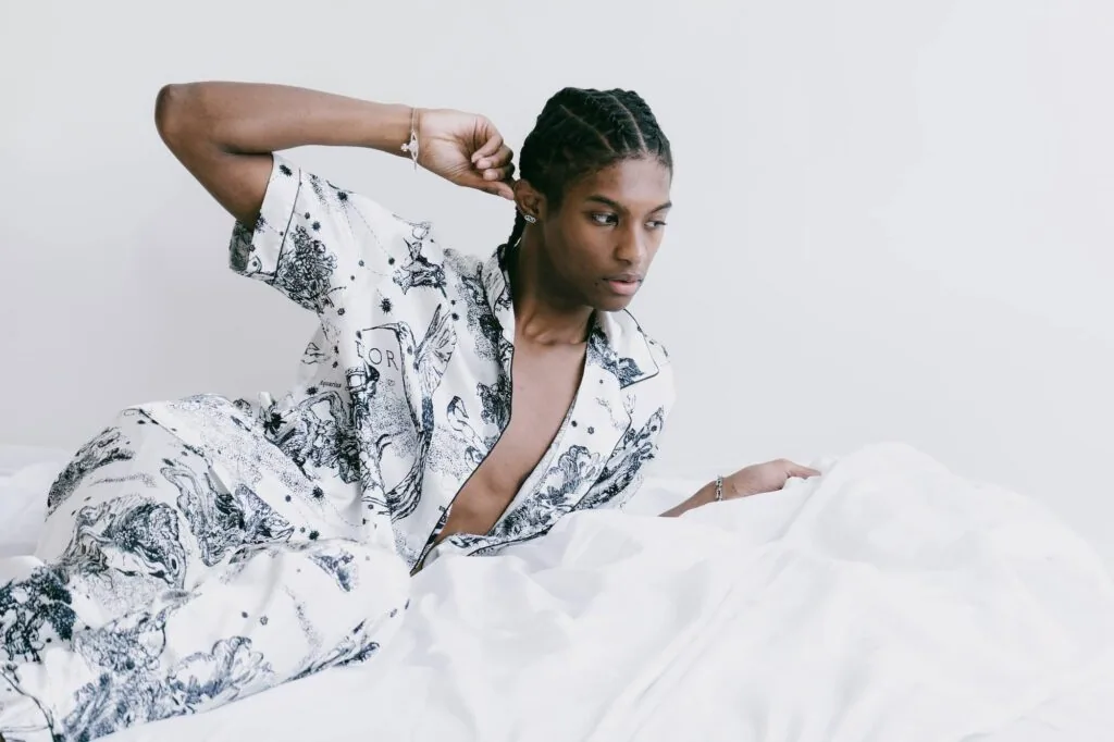Woman in white patterned blazer reclining against white background with arm raised, wearing rings