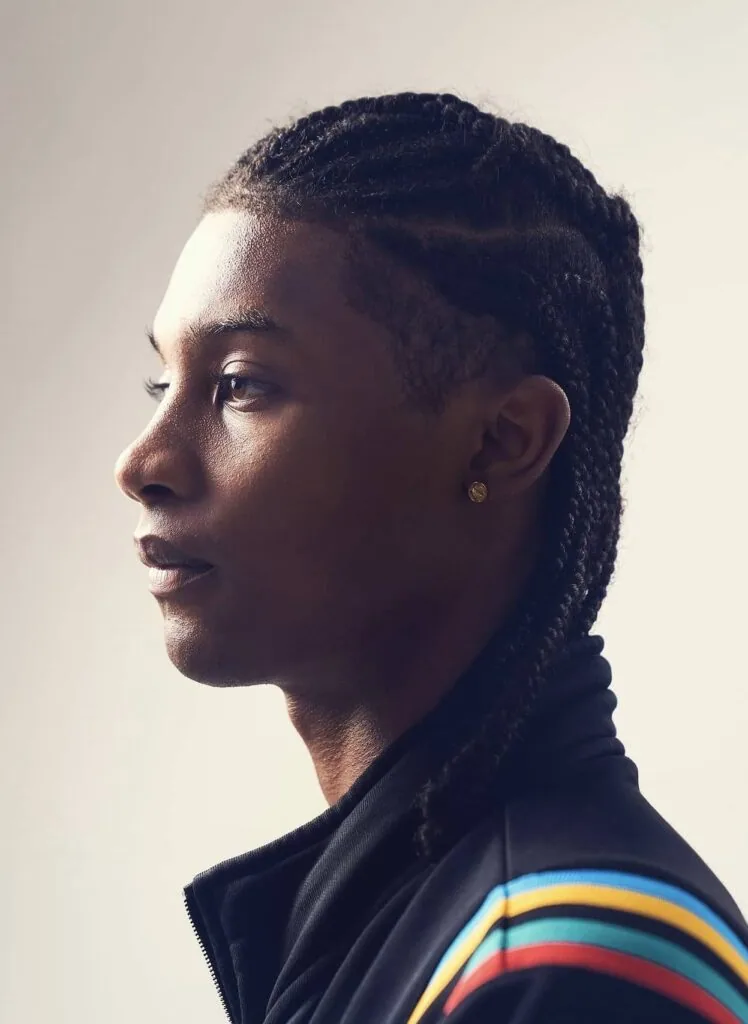 Male model in profile wearing black jacket with colorful striped sleeve detail and gold earring against neutral background