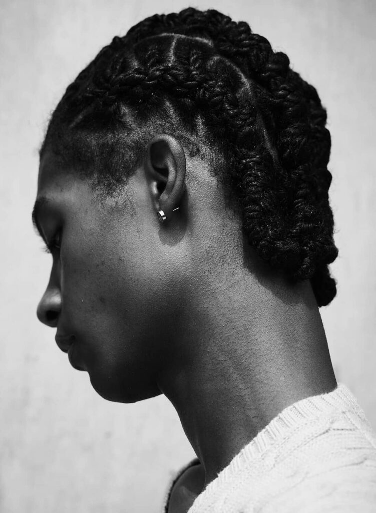 Male model profile view wearing white shirt, braided hairstyle, small earring, black and white portrait