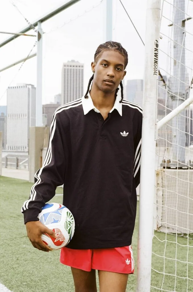 Person in black and white striped athletic polo holding soccer ball on rooftop sports field with city skyline background