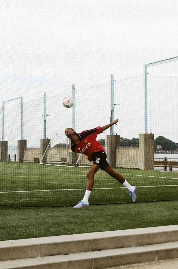 Soccer player in red jersey kicking ball on practice field with protective netting behind