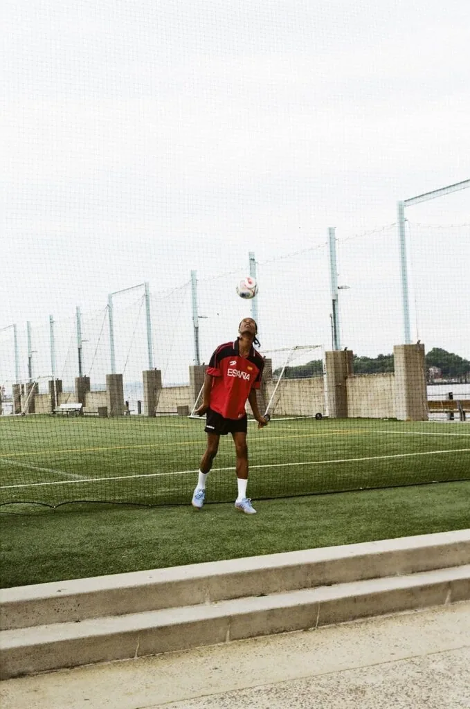 Soccer player in red jersey heading a ball on training field with safety nets