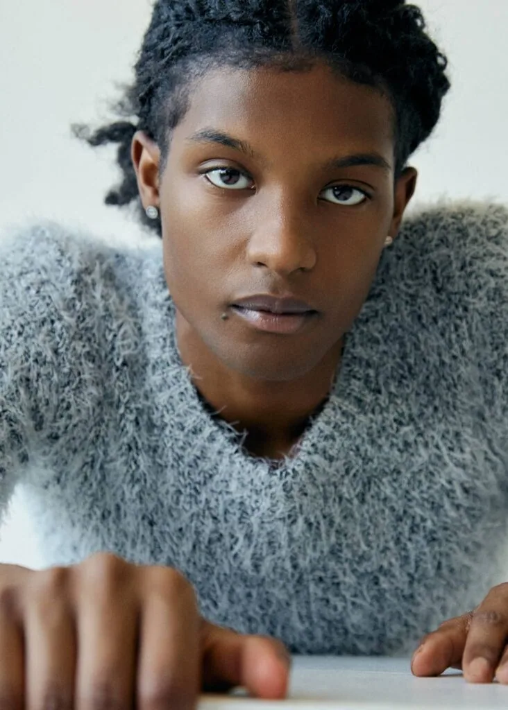 Person wearing gray knit sweater looking directly at camera with hands on surface