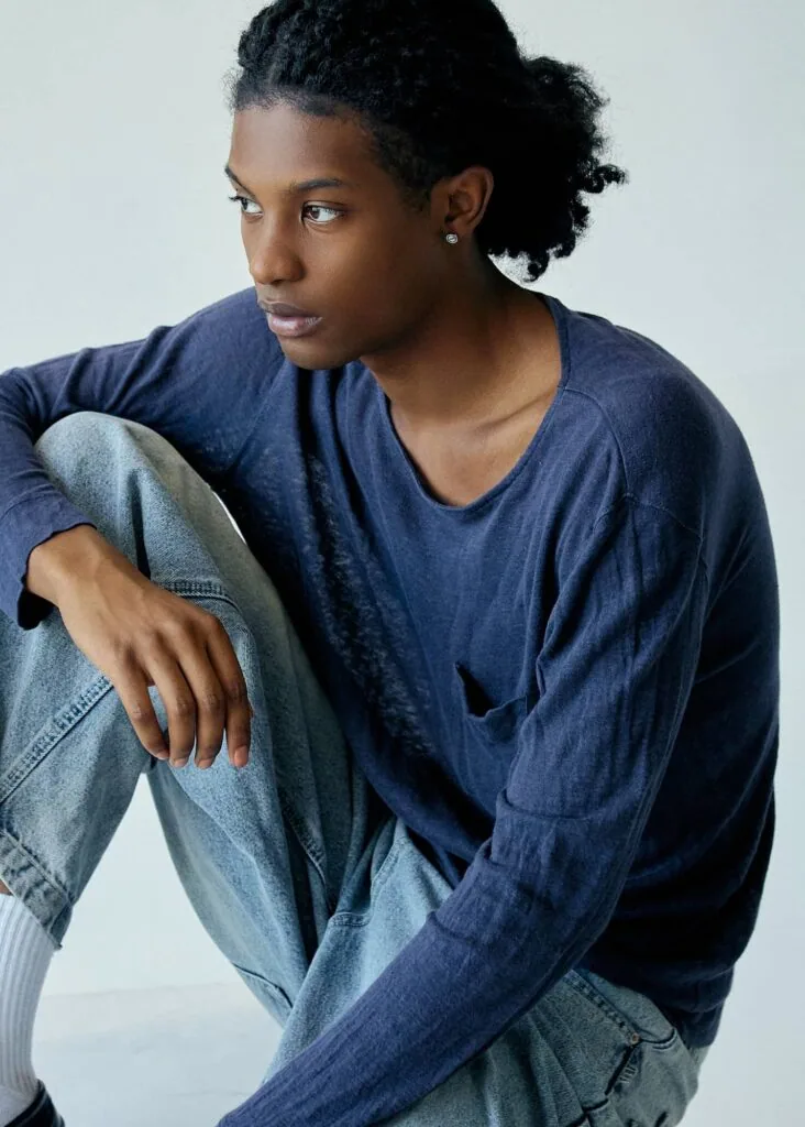 Person wearing navy blue v-neck shirt and light blue jeans, seated and gazing to the side against a light background