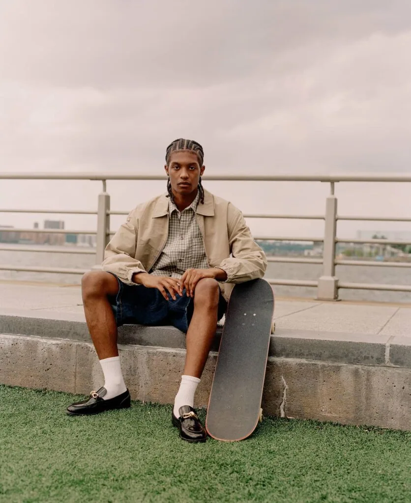 Man sitting on concrete ledge holding skateboard on rooftop with city skyline in background