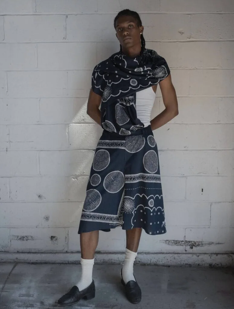 Person wearing navy and white patterned ensemble with white socks and black shoes against white brick wall