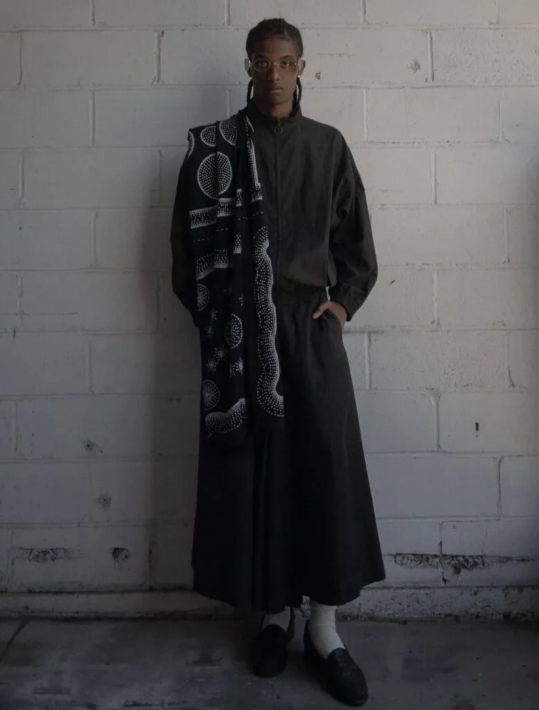 Person wearing black dress with geometric patterned scarf against white brick wall